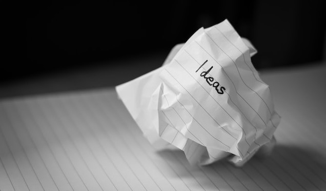 ασπρόμαυρη φωτογραφία τσαλακωμένης μπάλας χαρτιού με ιδέες γραμμένες πάνω της