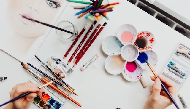 mains utilisant plusieurs pinceaux pour peindre le visage d'une femme à l'aquarelle