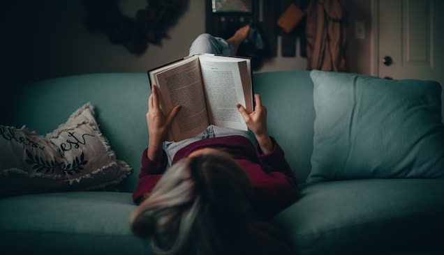 kobieta leżąca na kanapie i czytająca książkę