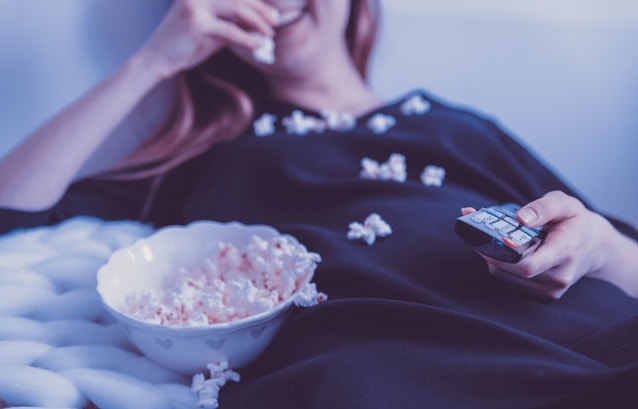 kvinna skrattar äter popcorn tittar på tv
